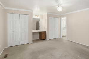 Unfurnished bedroom with ensuite bathroom, multiple closets, crown molding, light carpet, and built in desk