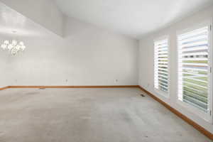 Unfurnished room with lofted ceiling, light colored carpet, and a chandelier
