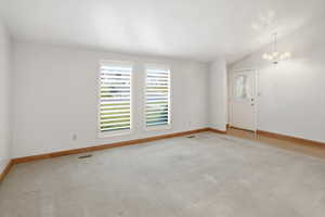 Empty room with vaulted ceiling, a chandelier, and carpet floors