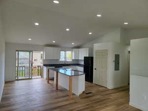 Kitchen with white cabinetry, a center island, vaulted ceiling, freestanding refrigerator, and dark wood-style flooring
