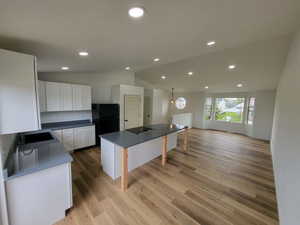 Kitchen with vaulted ceiling, white cabinetry, dark countertops, a breakfast bar area, and a kitchen island