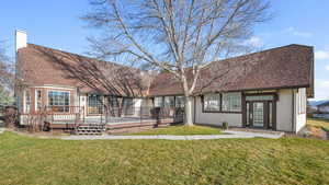 Back of house featuring a lawn, a wooden deck, a chimney, and a shingled roof