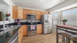 Kitchen with stainless steel appliances, light wood-style flooring, light brown cabinetry, dark stone countertops, and a textured ceiling