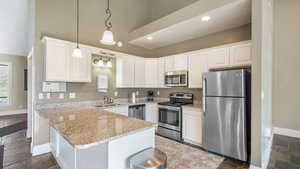 Kitchen featuring stone tile flooring, stainless steel appliances, a peninsula, decorative light fixtures, and light stone countertops