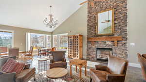 Living area with high vaulted ceiling, a fireplace, stone tile floors, ceiling fan, and a chandelier