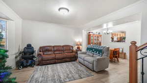 Living room featuring a textured ceiling, crown molding, light wood-style flooring, stairs, and a chandelier