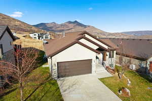 View of front of home with a front lawn, concrete driveway, stone siding, a mountain view, and a garage
