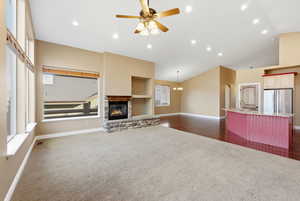 Unfurnished living room with lofted ceiling, a stone fireplace, a ceiling fan, dark colored carpet, and recessed lighting
