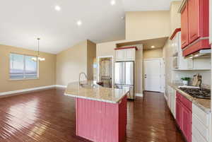 Kitchen with an island with sink, dark wood-type flooring, light stone countertops, pendant lighting, and freestanding refrigerator