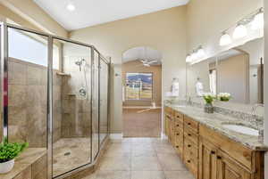 Bathroom featuring double vanity, ceiling fan, a stall shower, light tile patterned floors, and vaulted ceiling