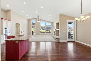 Kitchen featuring dark stone counters, open floor plan, a chandelier, arched walkways, and an island with sink