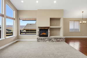 Unfurnished living room with healthy amount of natural light, a stone fireplace, a chandelier, built in features, and recessed lighting