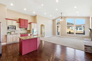 Kitchen with open floor plan, high vaulted ceiling, arched walkways, light stone countertops, and ceiling fan