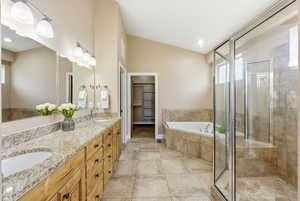Bathroom with a bath, double vanity, a walk in closet, vaulted ceiling, and a shower stall