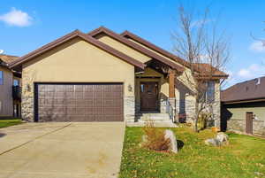 View of front of property featuring stucco siding, stone siding, an attached garage, driveway, and a front yard