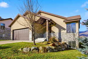 View of front of house featuring stone siding, stucco siding, driveway, an attached garage, and a front yard