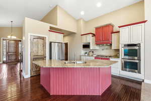 Kitchen with appliances with stainless steel finishes, high vaulted ceiling, light stone countertops, a chandelier, and an island with sink