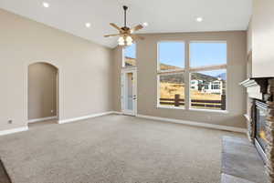 Unfurnished living room with a stone fireplace, light carpet, arched walkways, high vaulted ceiling, and a ceiling fan