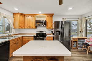 Kitchen featuring black appliances, light wood-type flooring, a kitchen island, light countertops, and brown cabinetry