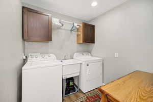 Laundry area featuring washing machine and dryer, cabinet space, and wood finished floors