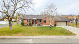 Single story home featuring a front lawn, driveway, brick siding, and a garage