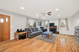 Living area with light wood-type flooring, a glass covered fireplace, healthy amount of natural light, a ceiling fan, and recessed lighting