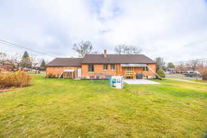 Back of house with brick siding, a chimney, and a yard