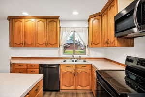 Kitchen with black range with electric cooktop, stainless steel microwave, dishwashing machine, brown cabinetry, and light countertops