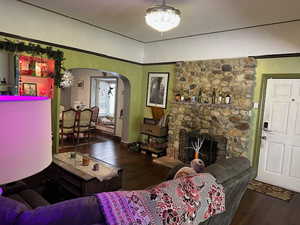 Living room with arched walkways, dark wood-style floors, and a stone fireplace