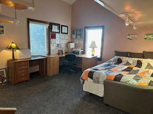 Bedroom featuring rail lighting, an office area, dark carpet, and lofted ceiling