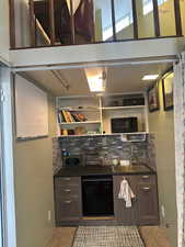 Kitchen featuring dark countertops, decorative backsplash, black appliances, open shelves, and dark brown cabinetry