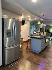 Kitchen with arched walkways, stainless steel fridge with ice dispenser, gray cabinets, hanging light fixtures, and dark wood finished floors