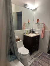 Bathroom with tile walls, vanity, a wainscoted wall, and light tile patterned floors