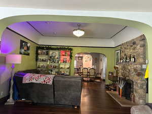 Living area featuring arched walkways, dark wood-style floors, and a stone fireplace