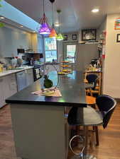 Kitchen with dark wood-style flooring, a kitchen island, recessed lighting, appliances with stainless steel finishes, and a kitchen bar