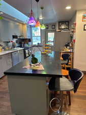 Kitchen with dark wood-style flooring, a kitchen island, recessed lighting, appliances with stainless steel finishes, and a kitchen bar