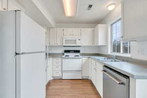 Kitchen featuring white appliances, white cabinetry, light wood-style floors, and light countertops