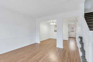 Unfurnished living room with stairs, a chandelier, light wood-style floors, and ornamental molding