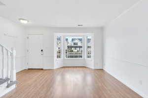 Entryway with stairway, light wood finished floors, and ornamental molding