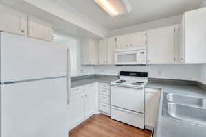 Kitchen with white appliances, white cabinets, and light wood finished floors