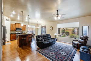 Living area with a chandelier, ceiling fan, light wood-style floors, and a textured ceiling