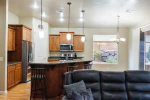 Kitchen featuring dark stone countertops, pendant lighting, a kitchen breakfast bar, appliances with stainless steel finishes, and open floor plan
