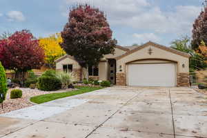 View of front facade with stone siding, driveway, stucco siding, and an attached garage
