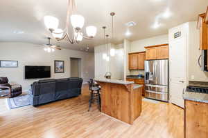 Kitchen featuring hanging light fixtures, a kitchen bar, a kitchen island with sink, stainless steel appliances, and brown cabinetry