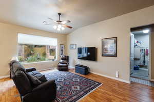 Living room with a ceiling fan, vaulted ceiling, and light wood-style floors