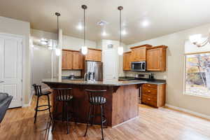 Kitchen featuring a kitchen breakfast bar, dark stone counters, decorative light fixtures, stainless steel appliances, and brown cabinetry