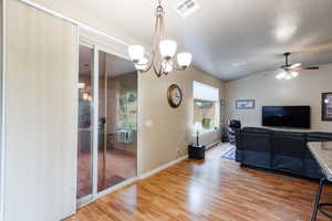 Living area featuring vaulted ceiling, light wood-type flooring, ceiling fan, and a chandelier
