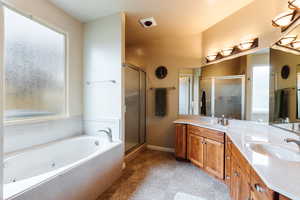 Bathroom with double vanity, a tub with jets, and a stall shower