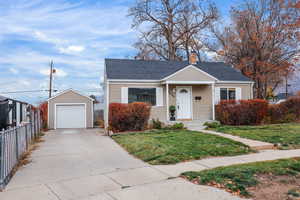 Bungalow-style house featuring an outbuilding, concrete driveway, a shingled roof, a chimney, and a detached garage