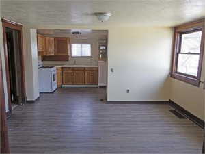 Kitchen with brown cabinetry, white gas range oven, dark wood-style floors, a textured ceiling, and light countertops